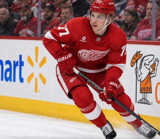 Simon Edvinsson skating for the Detroit Red Wings amid Philadelphia Flyers trade rumors, with Walmart and Little Caesars ads on the boards.