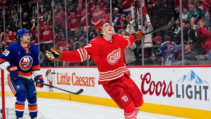 simon-edvinsson-islanders-red-wings-trade-rumors Simon Edvinsson of the Detroit Red Wings celebrates a goal beside New York Islanders defenseman Alexander Romanov as NHL trade rumors swirl around a potential $9 million Islanders offer sheet.
